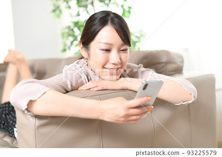 A woman operating a smartphone with a sofa A woman operating a smartphone with a sofa 93225579