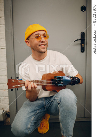 Young disabled man with artificial prosthetic hand plays on Ukulele guitar at shop Young disabled man with artificial prosthetic hand plays on Ukulele guitar at shop 93225976