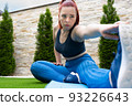 young girl training in sports clothes, stretching her legs on a mat in the garden of her house. Training of a sportswoman. Concept of health and well-being. 93226643