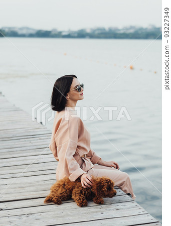 Brunette woman sitting on pier with her redhead dog toy poodle 93227349