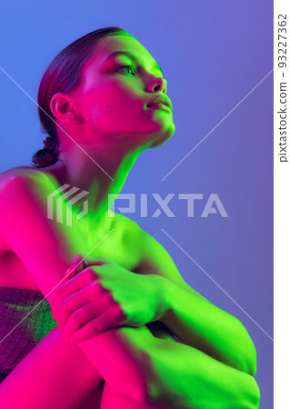 Portrait of young, beautiful and healthy girl with well-kept skin isolated on dark background in neon light. Art, fashion, style, facial expression 93227362