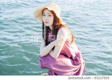 A woman with a straw hat looking at you at the beach 93227850