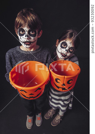 Two kids holding pumpkin buckets at Halloween 93230092