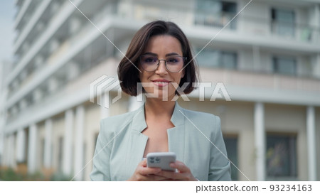 Portrait view of the happy woman looking into mobile phone screen while chatting online in city street Portrait view of the happy woman looking into mobile phone screen while chatting online in city street 93234163