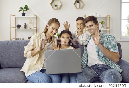 Happy family sitting on the couch, making a video call and waving hello at the laptop PC Happy family sitting on the couch, making a video call and waving hello at the laptop PC 93234205