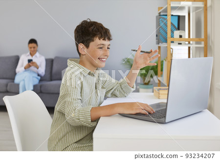 Cheerful boy who studies at home is talking to teacher or tutor using video call. Cheerful boy who studies at home is talking to teacher or tutor using video call. 93234207