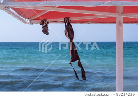 Marine background. On the beach, a swimsuit bra and shorts are hung under an umbrella. vacation freedom concept Marine background. On the beach, a swimsuit bra and shorts are hung under an umbrella. vacation freedom concept 93234239