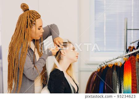 Hairstylist braided afro braids dreadlocks kanekalon pigtails hair of female client in barber salon. Hairstylist braided afro braids dreadlocks kanekalon pigtails hair of female client in barber salon. 93234623