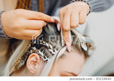 Hairstylist braided afro braids dreadlocks kanekalon pigtails hair of female client in barber salon. Hairstylist braided afro braids dreadlocks kanekalon pigtails hair of female client in barber salon. 93234640