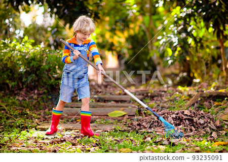 Child and rake in autumn garden. Kid raking leaves 93235091