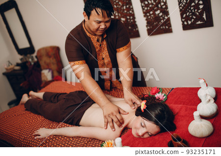 Thai man making classical thai massage procedure to young woman at beauty spa salon 93235171