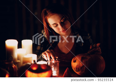 Young woman making Halloween pumpkin Jack-o-lantern with candles in dark. Female hands cutting pumpkins with knife Young woman making Halloween pumpkin Jack-o-lantern with candles in dark. Female hands cutting pumpkins with knife 93235514