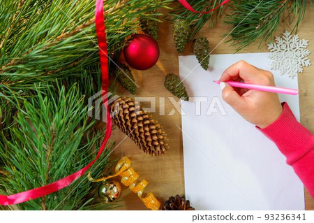 Young woman writes a New Year's greeting card or Christmas wish sheet on a white piece of paper. Young woman writes a New Year's greeting card or Christmas wish sheet on a white piece of paper. 93236341