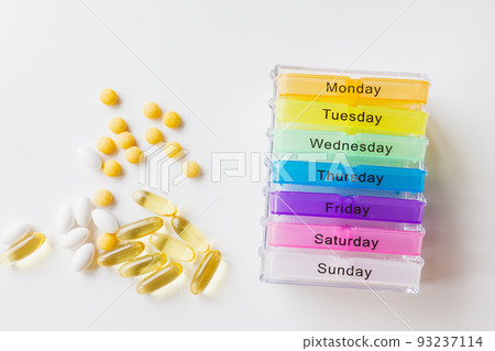 Week medicine dispenser. Plastic seven day weekly container with different white and yellow pills on white background. Top view, copy space 93237114