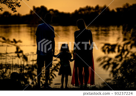 silhouette of a family watching the sunset on the shore of a lake 93237224
