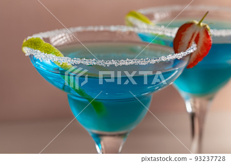 Two glasses with blue margarita cocktail garnished with lime zest and strawberries, selective focus 93237728