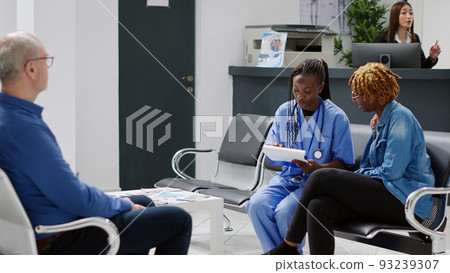 Medical assistant doing consultation with patient in hospital reception lobby, sitting in waiting room and talking about healthcare or treatment. Nurse giving advice to young adult. Medical assistant doing consultation with patient in hospital reception lobby, sitting in waiting room and talking about healthcare or treatment. Nurse giving advice to young adult. 93239307