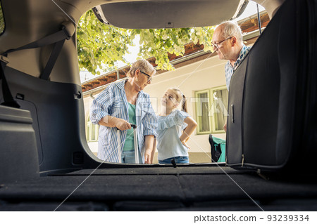 Grandparents and niece leaving on vacation, loading travel bags and baggage in automobile trunk. Senior people and little kid travelling on summer holiday road trip with vehicle, drive journey. Grandparents and niece leaving on vacation, loading travel bags and baggage in automobile trunk. Senior people and little kid travelling on summer holiday road trip with vehicle, drive journey. 93239334