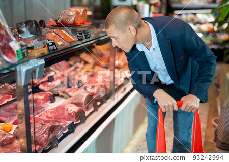 Focused man examines the production in the department of the butcher shop in the supermarket Focused man examines the production in the department of the butcher shop in the supermarket 93242994