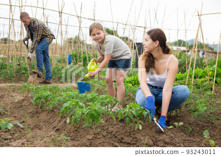 Mother and daughter watering plants at garden closeup Mother and daughter watering plants at garden closeup 93243011