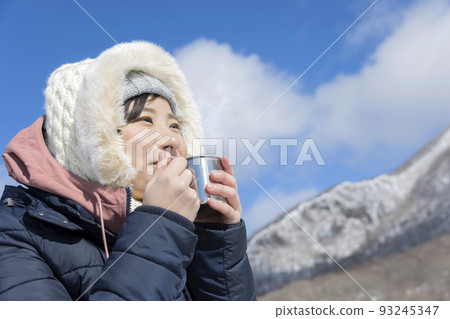 Young woman drinking hot drink in mug in winter mountains 93245347