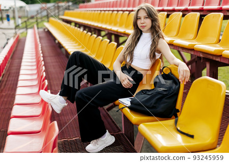 A smiling teenage girl is sitting on the podium next to her school backpack A smiling teenage girl is sitting on the podium next to her school backpack 93245959