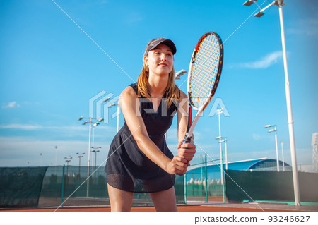 A beautiful young woman plays tennis on the court. Sporting black dress suit. The girl smiles, happy. The athlete delivers the ball. Team play, training, active outdoor lifestyle portrait A beautiful young woman plays tennis on the court. Sporting black dress suit. The girl smiles, happy. The athlete delivers the ball. Team play, training, active outdoor lifestyle portrait 93246627