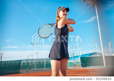 A beautiful young woman plays tennis on the court. Sporting black dress suit. The girl smiles, happy. The athlete delivers the ball. Team play, training, active outdoor lifestyle A beautiful young woman plays tennis on the court. Sporting black dress suit. The girl smiles, happy. The athlete delivers the ball. Team play, training, active outdoor lifestyle 93246628