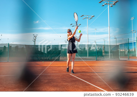 A beautiful young woman plays tennis on the court. Sunlight, training, competition. Outdoor sports, team play. Active lifestyle, athlete with a racket and a ball 93246639