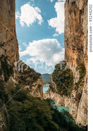 Blue sky with clouds between narrow rocky cliffs. River in Congost de Mont Rebei gorge in Catalonia, Spain. Natural border between Catalonia and Aragon. 93248202