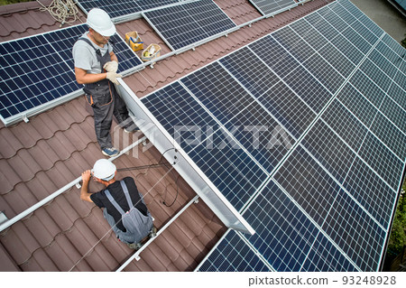 Man technician mounting photovoltaic solar moduls on roof of house. Mounter in helmet installing solar panel system outdoors. Concept of alternative and renewable energy. Aerial view. 93248928