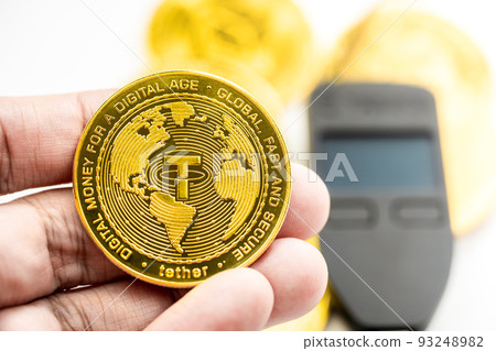 Hand holding a Stable Cryptocurrency USDT coin with hardware wallet in background. Hand holding a Stable Cryptocurrency USDT coin with hardware wallet in background. 93248982