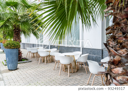 Street cafe with white chairs, green foliage around. Without people, tourism, travel. 93249317