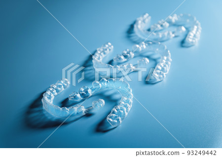 Close up invisible aligners on blue background with copy space. Plastic braces for teeth alignment. Set of three pairs of aligners on a blue background 93249442
