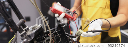 Mechanic using multimeter checks voltage level motorcycle battery motorcycle garage 93250574