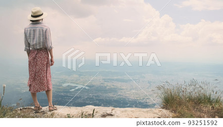 Traveler enjoying city view on mountain top. Happy woman traveler stands on mountain top, looks at scenery view of Tirana city, Albania. Dream travel concept, inspiration. Free wind blows girl's dress 93251592