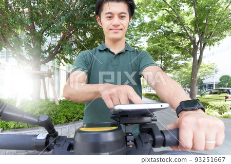一個年輕人操作連接到踢板/自行車的智能手機 一個年輕人操作連接到踢板/自行車的智能手機 93251667