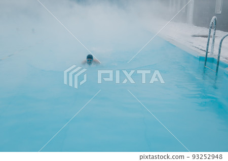 Fit swimmer male training swim in open winter swimming pool with fog. Geothermal outdoor spa health concept. 93252948