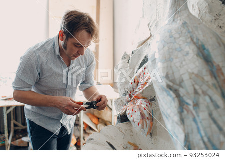 Workplace mosaics master making smalt glass mosaic panel. Man mosaicist at work 93253024