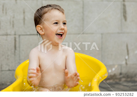 Cute little boy bathing in yellow tub outdoors. Happy child is splashing, playing with water and having fun. Summer season and recreation. Staying cool in the summer heat. Water fun in backyard. Cute little boy bathing in yellow tub outdoors. Happy child is splashing, playing with water and having fun. Summer season and recreation. Staying cool in the summer heat. Water fun in backyard. 93253282