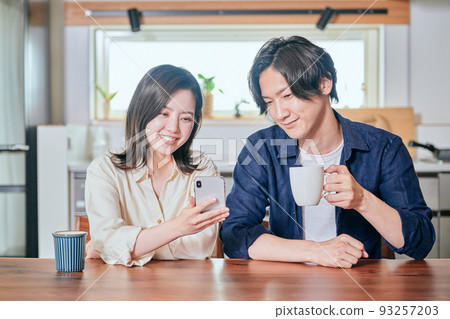 Young couple looking at smartphone while drinking coffee in dining kitchen 93257203