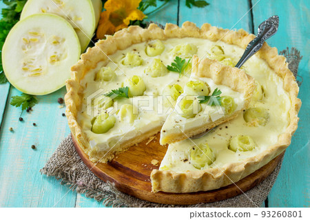 A classic quiche Lorraine pie with feta cheese with zucchini, egg pouring and cheese on a kitchen wooden table. 93260801