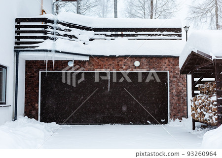 Automatic garage door of a cottage in a snowfall. Winter house with automatic garage doors. Mansion in the winter forest. Winter courtyard of a private cottage 93260964