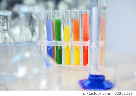 Focus on test tubes with rainbow colored chemicals and reagents standing on tripod. Blurred foreground with graduated cylinder, flasks and measuring glass labware. Chemistry, science concept Focus on test tubes with rainbow colored chemicals and reagents standing on tripod. Blurred foreground with graduated cylinder, flasks and measuring glass labware. Chemistry, science concept 93261156