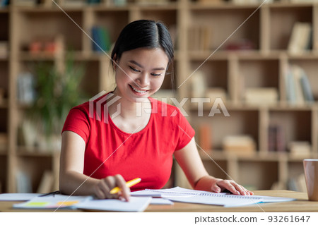 Glad cheerful pretty smart young asian lady student study at table alone in room or library interior Glad cheerful pretty smart young asian lady student study at table alone in room or library interior 93261647
