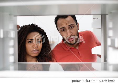 Hungry unhappy upset young african american woman and man check empty fridge in kitchen 93261668