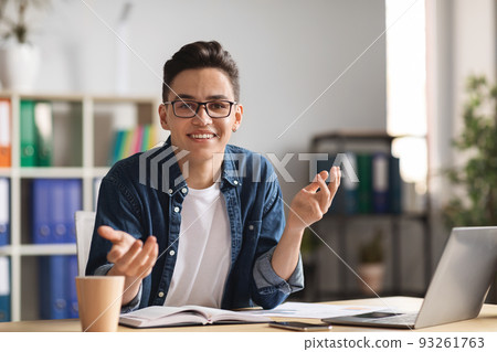 Handsome young male office employee sitting at desk and talking at camera 93261763