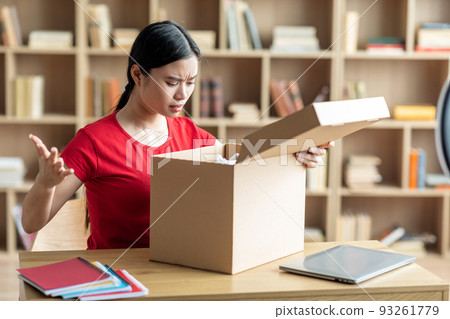 Frustrated disappointed young japanese lady opens cardboard box and sad for mistake with parcel 93261779