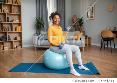Cheerful young pregnant african american female with big belly doing exercises with dumbbells on fit ball Cheerful young pregnant african american female with big belly doing exercises with dumbbells on fit ball 93261833
