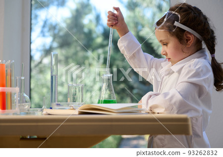 Side view of a Caucasian little girl chemist using pipette, dripping reagents into a flask with chemical liquid in the school laboratory. Learning Science and chemistry in new academic year semester Side view of a Caucasian little girl chemist using pipette, dripping reagents into a flask with chemical liquid in the school laboratory. Learning Science and chemistry in new academic year semester 93262832